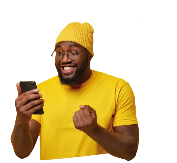A young man, wearing a yellow t-shirt and hat, is looking at his phone in his hand
and smiling. He is making a fist with his other hand.